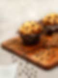 Two chocolate chip muffins, one with a bite taken out, on a wooden cutting board