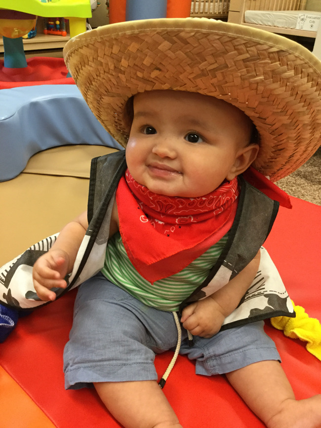 Little toddler boy smiles happily wearing in a sombrero and a scarf around his neck