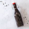 A closed bottle containing a dark liquid lays on a white marble countertop