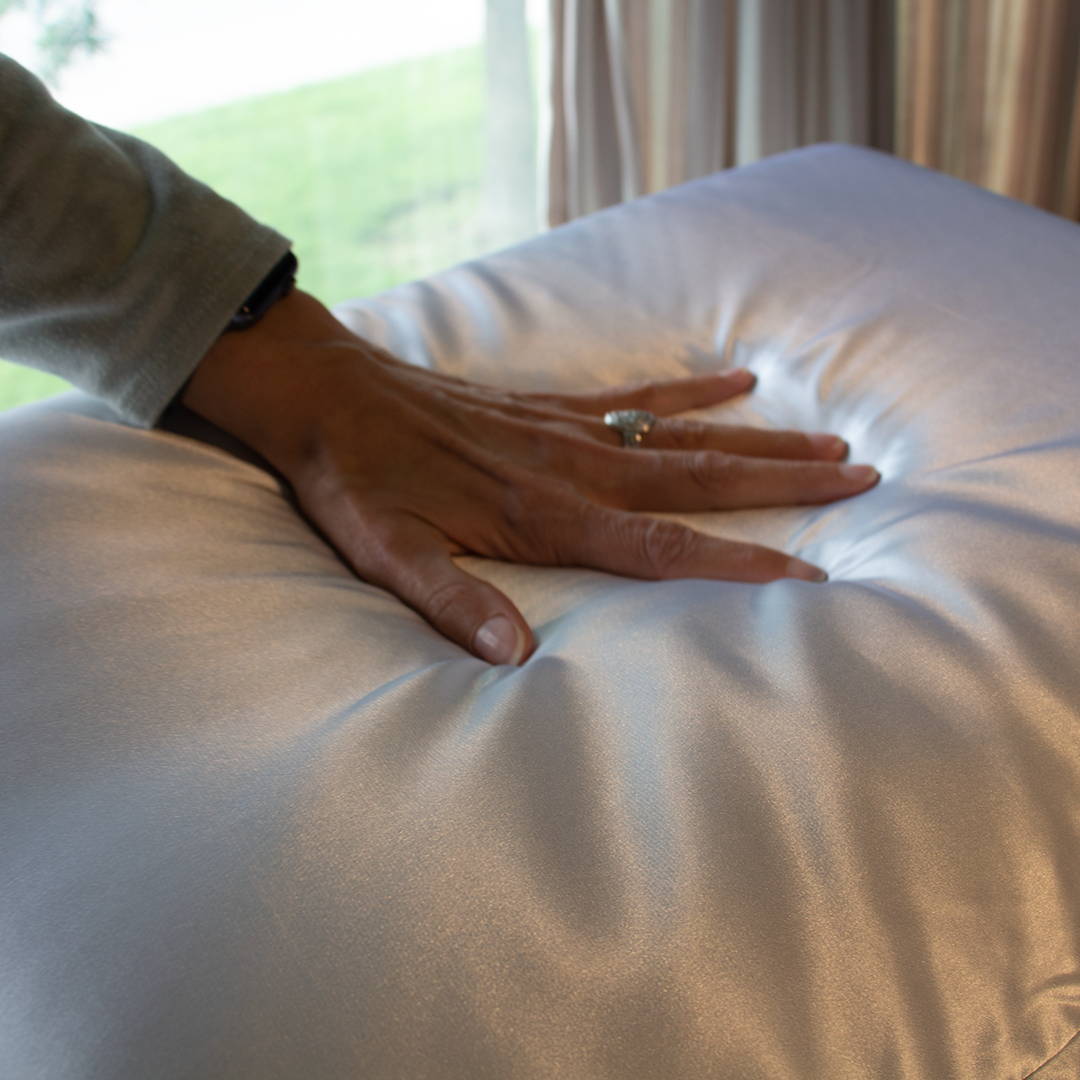 Womans hand feeling white silk pillowcase.