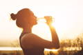 woman drinking water from a bottle at sunset 