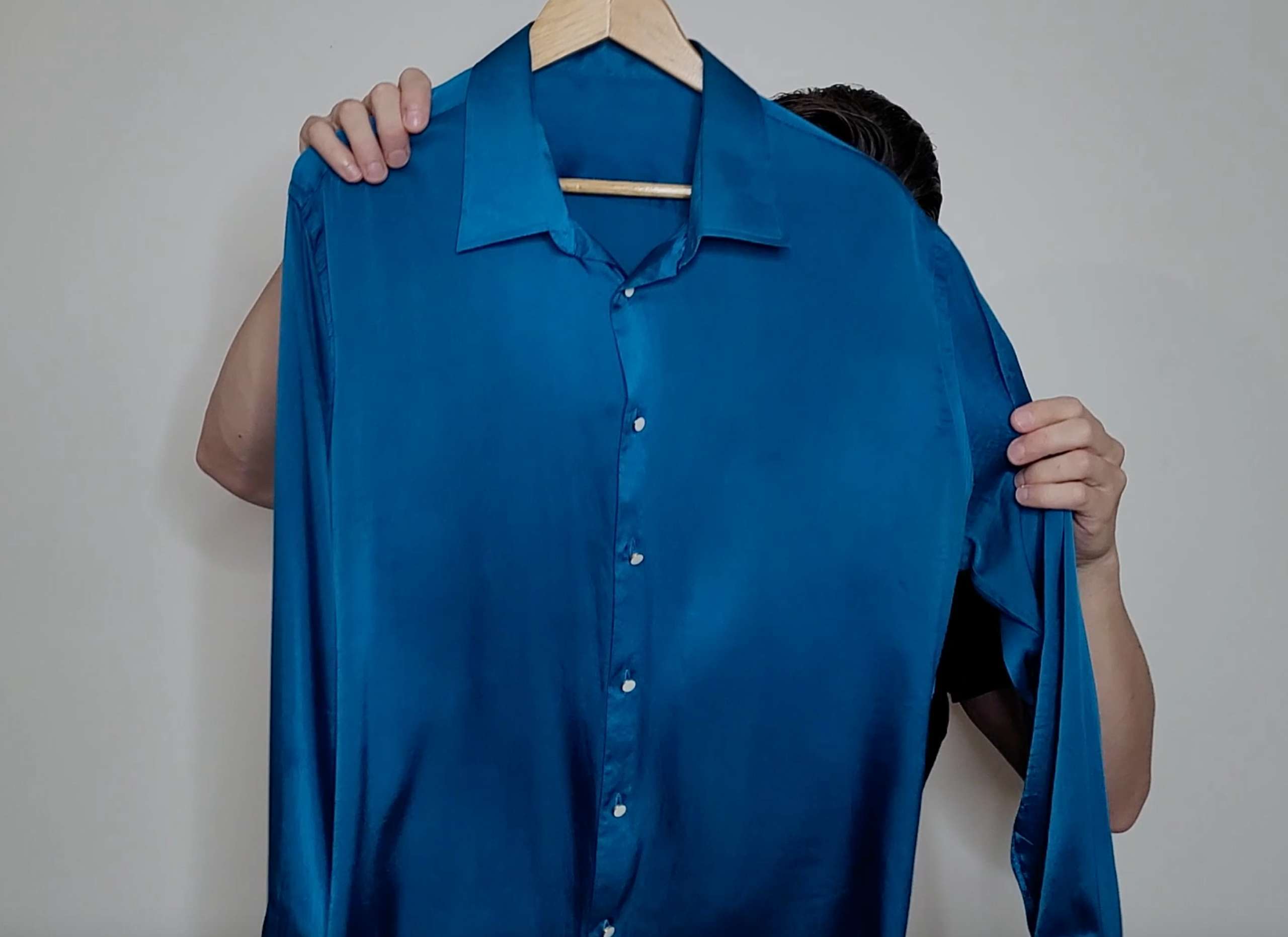 a photo of a man holding up a freshly pressed and wrinkle free blue silk shirt
