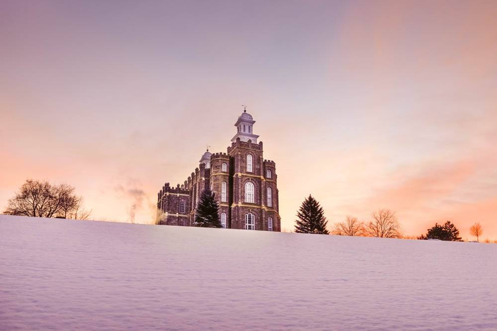 Logan Temple standing on a snowy hill with orange skies behind it. 