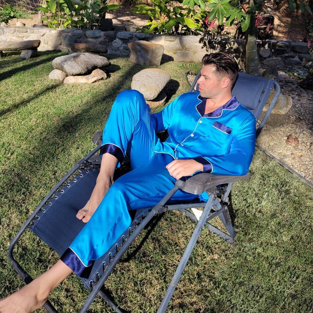 model setting in a chair outside basking in the sun and wearing a blue silk pajama set