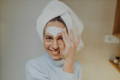 woman with a towel on her head applying face mask for clogged pores