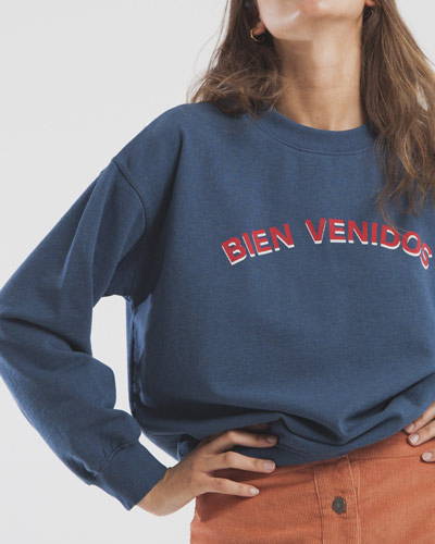 Woman wearing navy blue organic cotton sweatshirt with red printed logo from sustainable clothing brand Thinking Mu