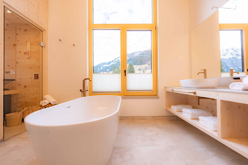 Helles Badezimmer mit freistehender Badewanne und Fensterblick auf die Berge in Mittelberg im Kleinwalsertal.