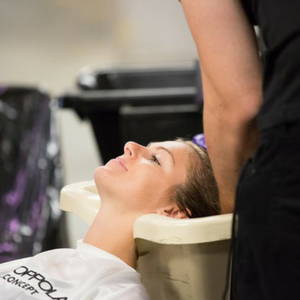 woman in a white cape leaning her head back as a hair stylist washes her hair