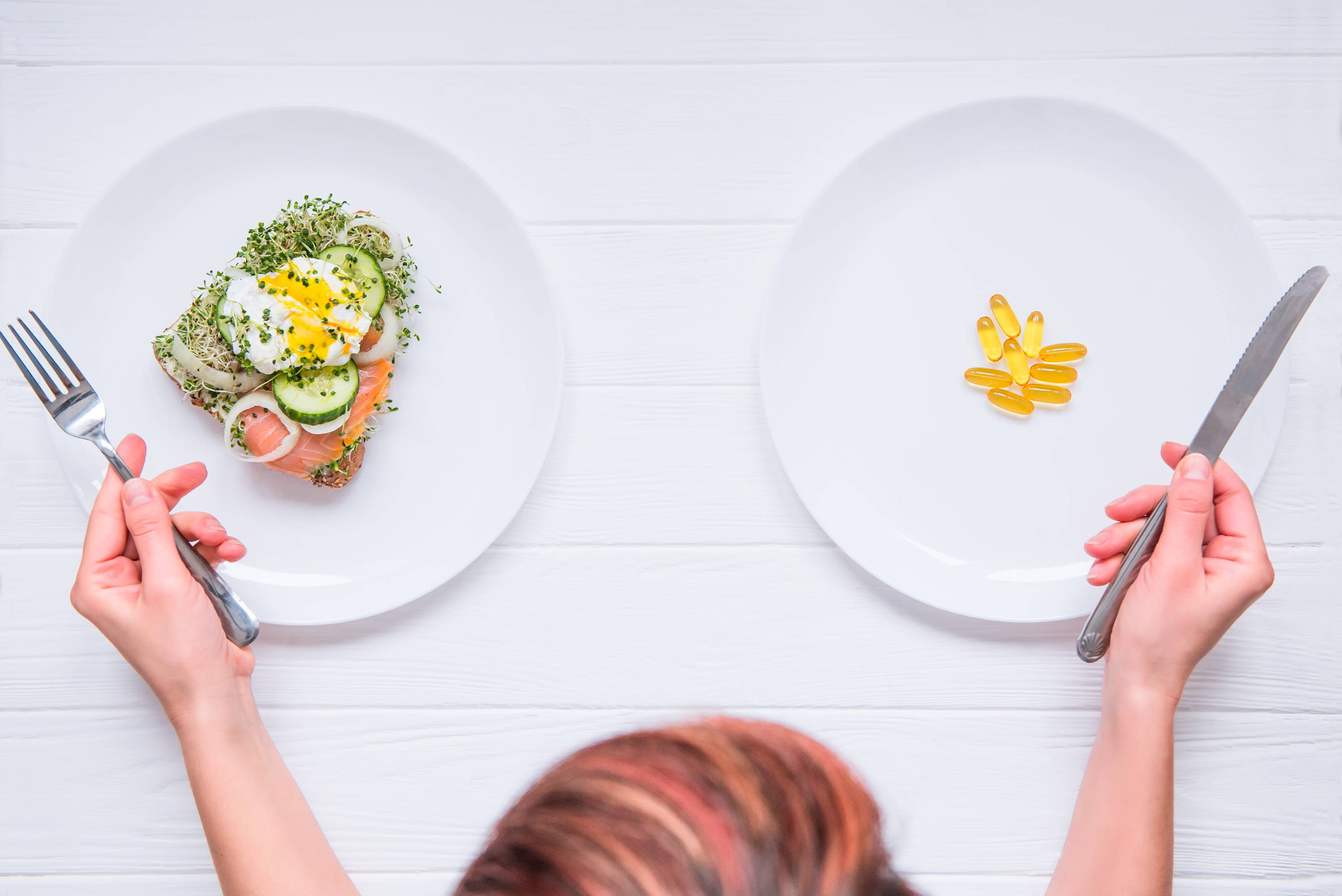 Woman looking at a plate of normal food and a plate full of additives comparing which is better to get nutrients from  
