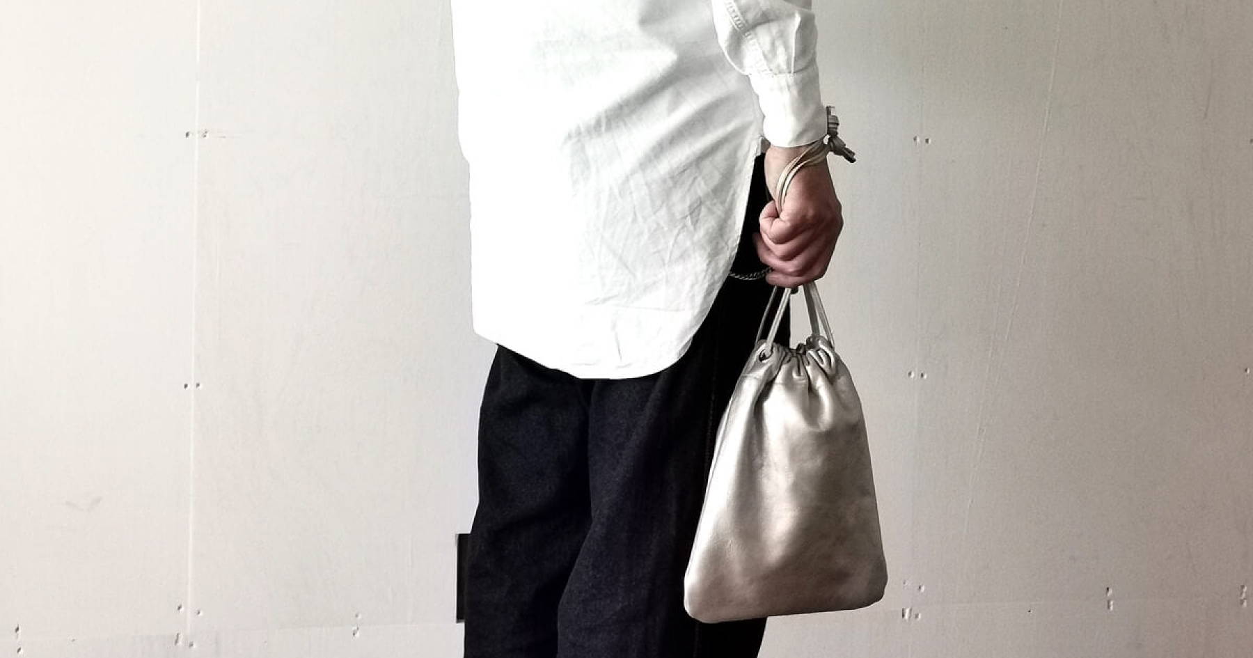 白いシャツに黒いズボンを履いた人がシルバーの巾着バッグを持っている。