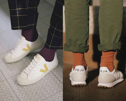 Vegan sneakers from Veja with man wearing white trainers with orange socks and green chinos and woman wearing sustainable Veja white pumps with purple socks and navy yellow checked trousers