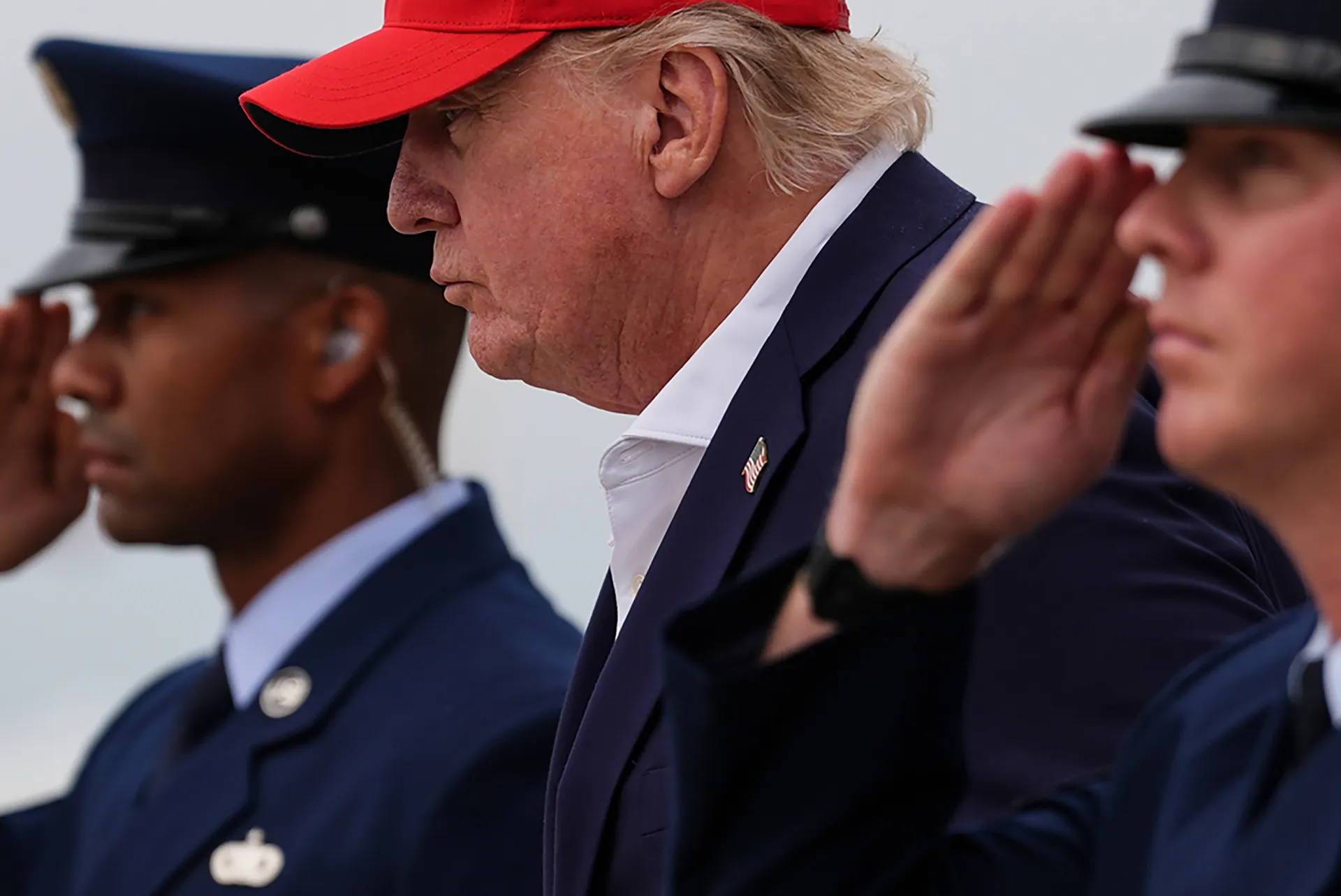 Donald Trump stands looking forward others around him salute.