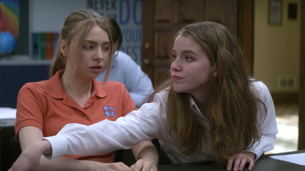 Sterling and April in a classroom. Sterling looks surprised as April deliberately reaches across her, allowing their arms to touch.