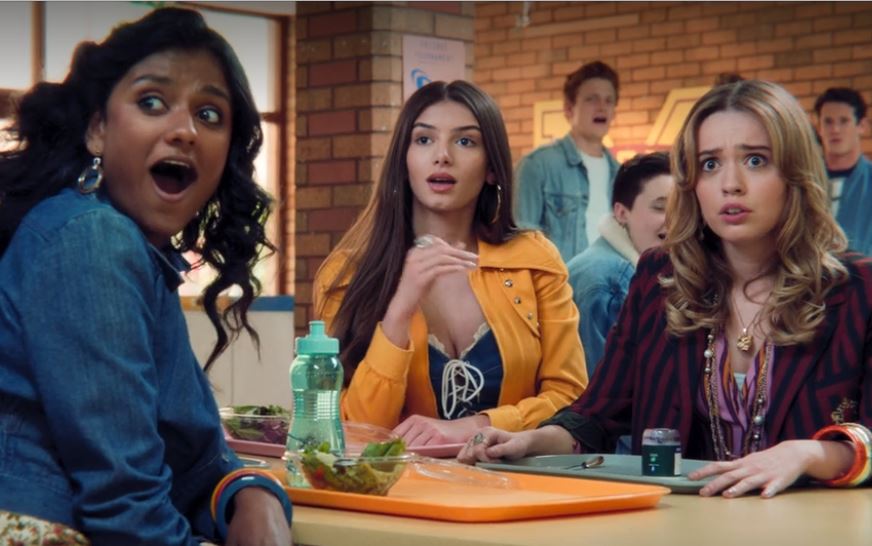 Ruby, Aimee, and Olivia sitting at a lunch table with shocked expressions on their face looking at someone off camera.