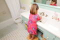 Little girl standing on a stool and washing her hands at the sink.