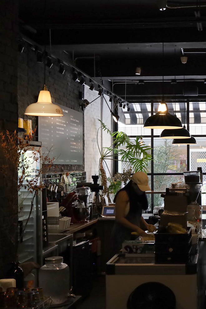 Two Terracotta lampshades hanging over a table in a coffee shop. Three District Line Black lampshades hang over the counter in the background