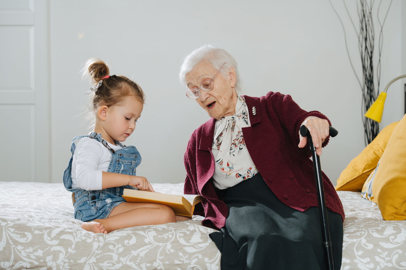 Great-grandma sitting on bed with great-grandchild. 