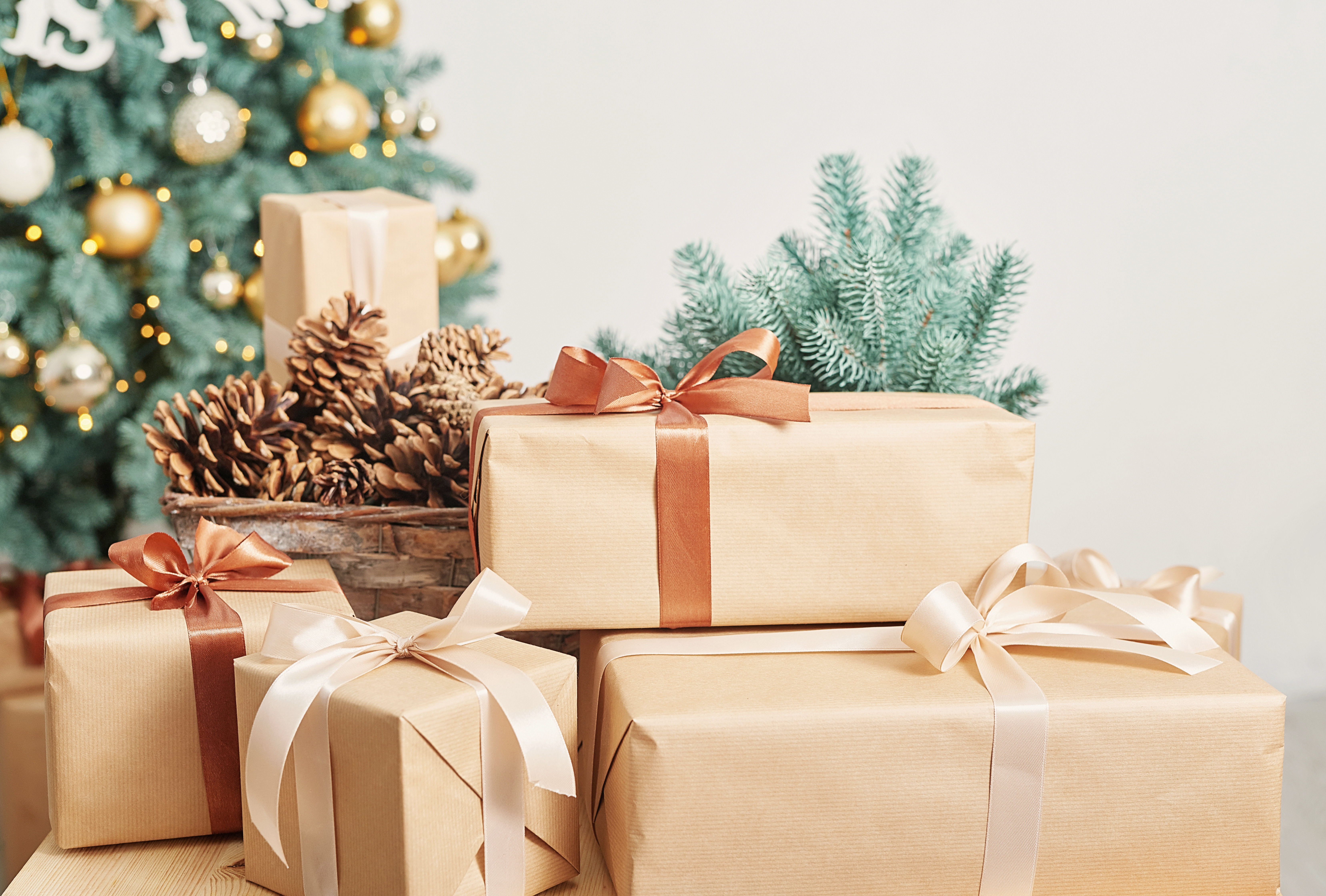 Christmas gifts wrapped in brown paper with satin bows beside a bowl of pinecones and a Christmas tree