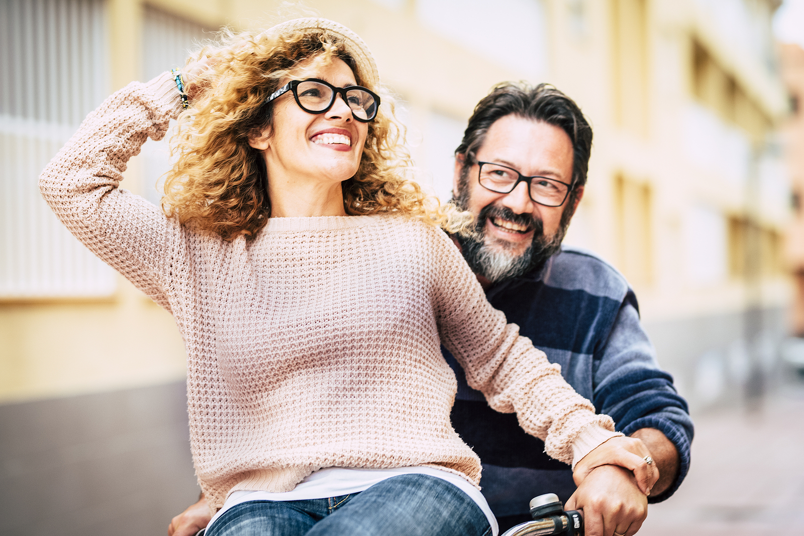 An older couple laughing while riding a bike together in the street.