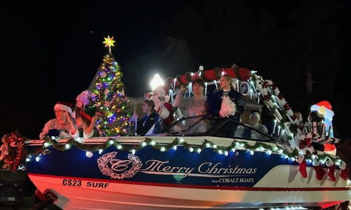 Festive boat adorned with Christmas lights and tree, with people in holiday attire, creating a joyful, celebratory atmosphere.