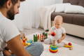 Father watching his baby playing with colorful Montessori stacking rings.