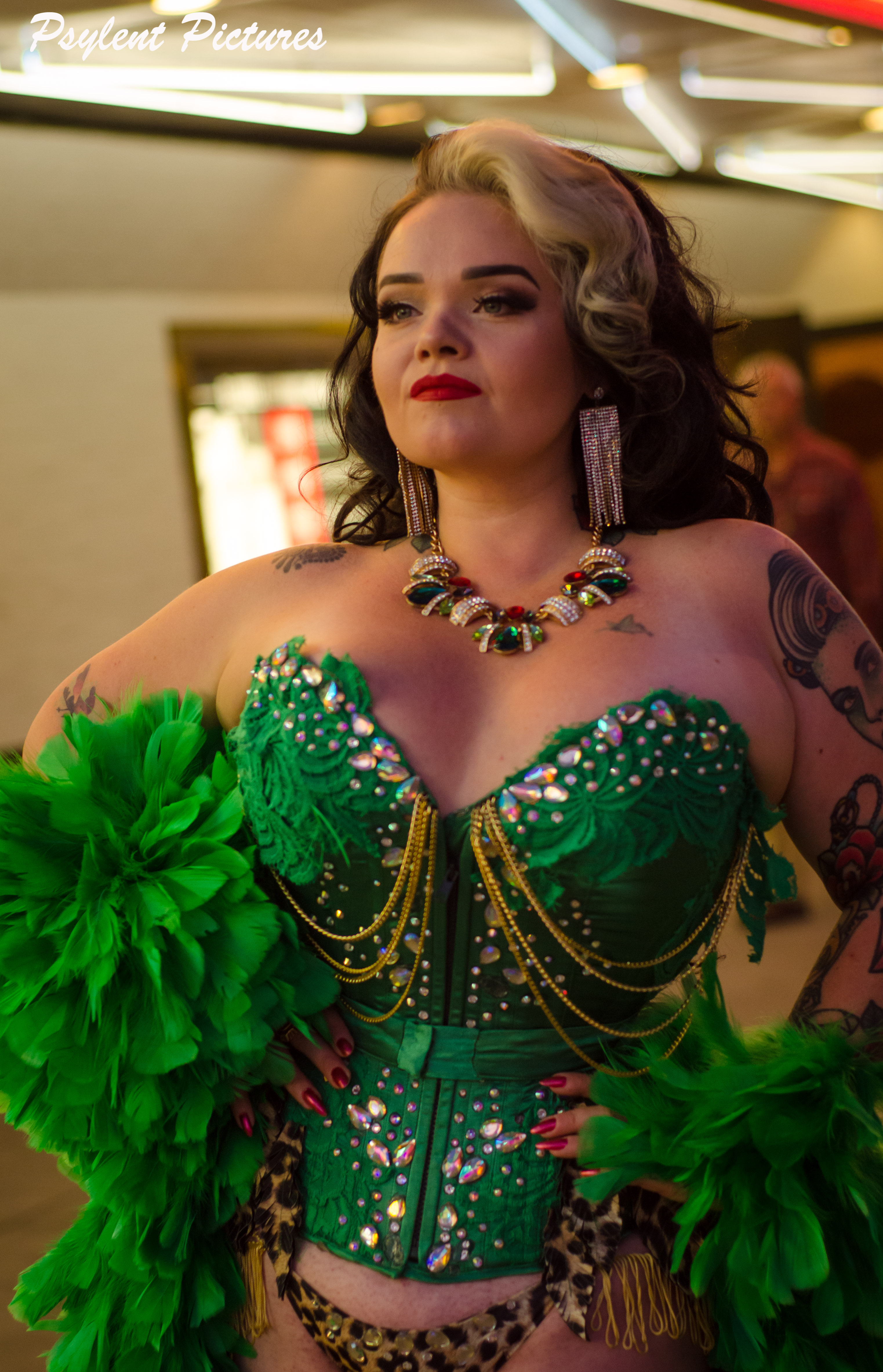 Molly with her arms on her waist wearing a bright colored corset looking in the mirror with a confident expression.
