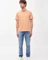 Man wearing orange and white striped organic cotton t-shirt with blue organic cotton denim jeans from Armedangels, a sustainable clothing brand making causal clothing in Cologne, Germany