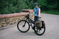 man standing next to and holding a bike with frost river bike bags on a bridge.