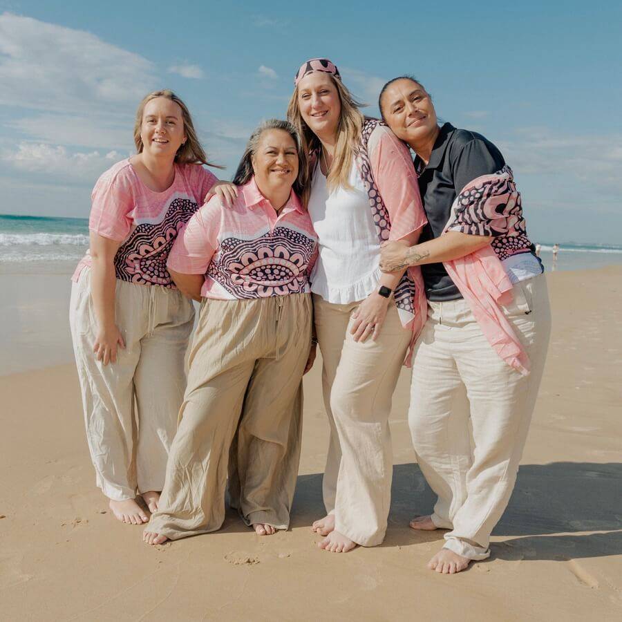 Kelly and three of her friends stood on the sand on the beach in front of the sea wearing Boobie Sista clothes 
