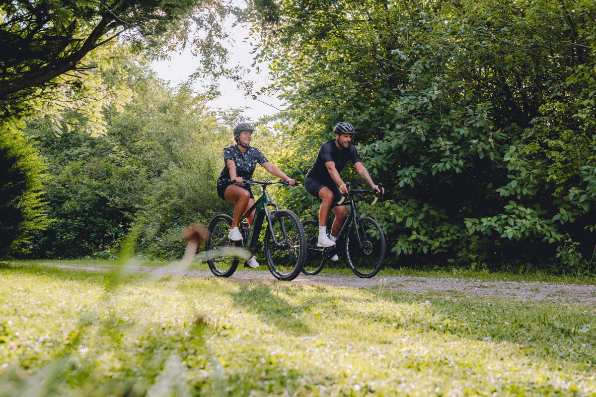 Ein Mann und eine Frau fahren in der Natur auf einem Kiesweg Fahrrad.