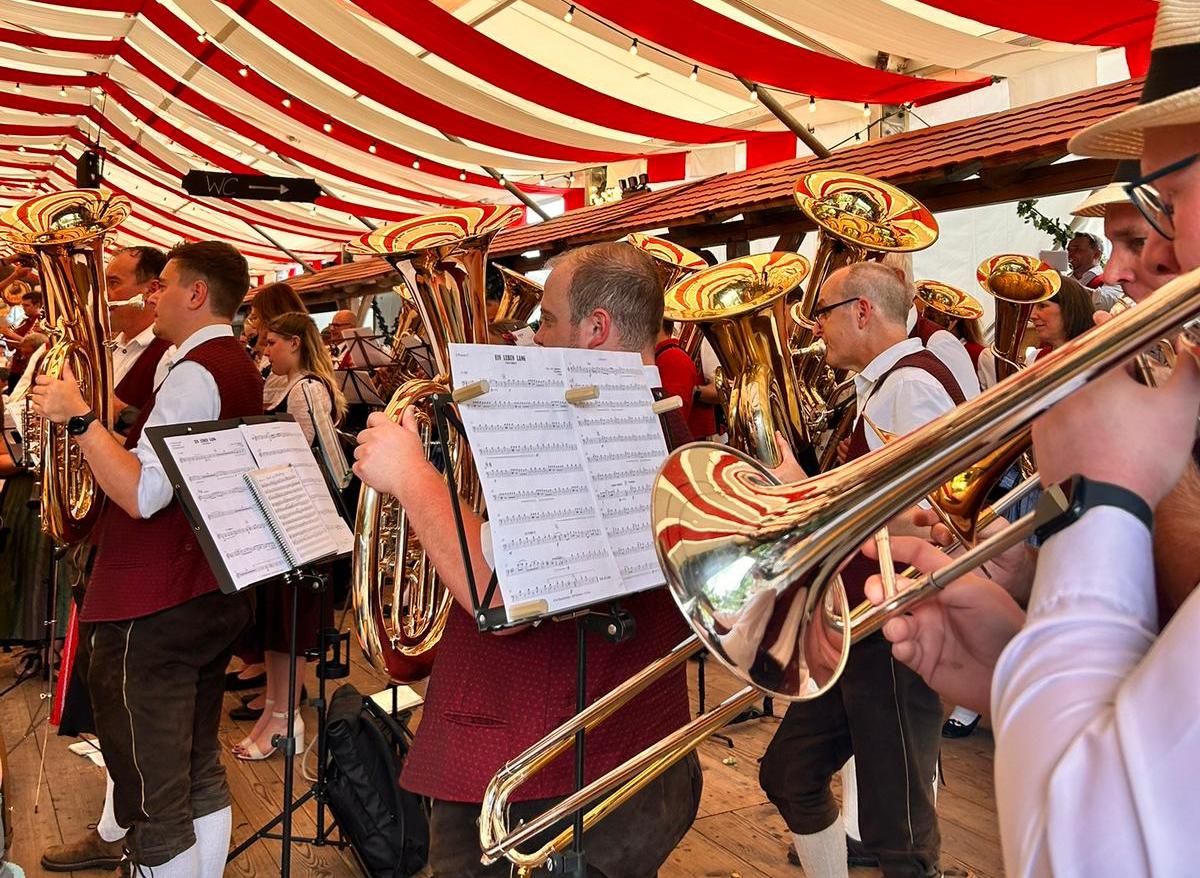 In einem Festzelt musizieren einige Musikerinnen und Musiker in Tracht gemeinsam. 