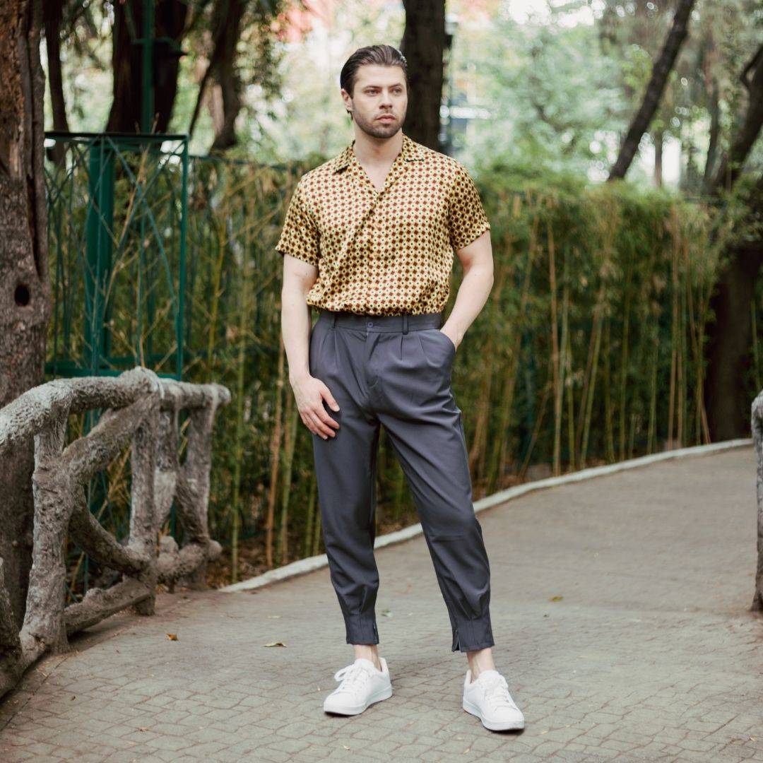 full body image of a model standing in the park wearing white shoes grey pants and a short sleeve gold bowling silk shirt from 1000 kingdoms