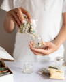 A person empties a plastic pouch labeled 'Caramom' into a glass spice jar by Gneiss Spice