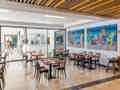 Heller, zwangloser Restaurantbereich mit ordentlich arrangierten Tischen, farbenfroher Cocktail-Kunst an der Wand und einer gläsernen Raumtrennung.