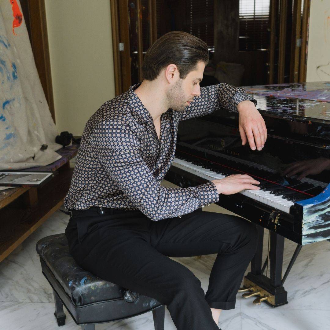 model sitting near a piano wearing black pants and a long sleeve navy grid silk shirt from 1000 kingdoms
