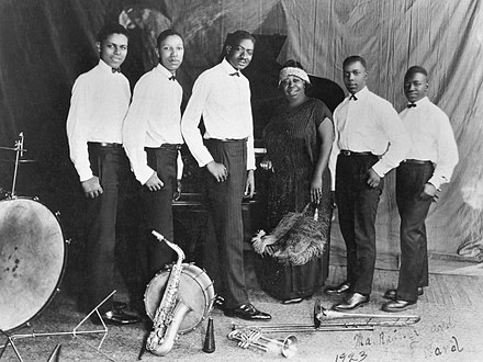Ma Rainey in the center with her band posing for a picture with their instruments at their feet.