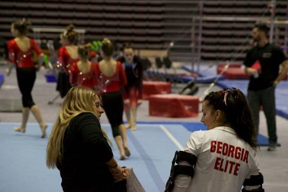 Emily's coach giving advice while she cheers on teammates at at meet.