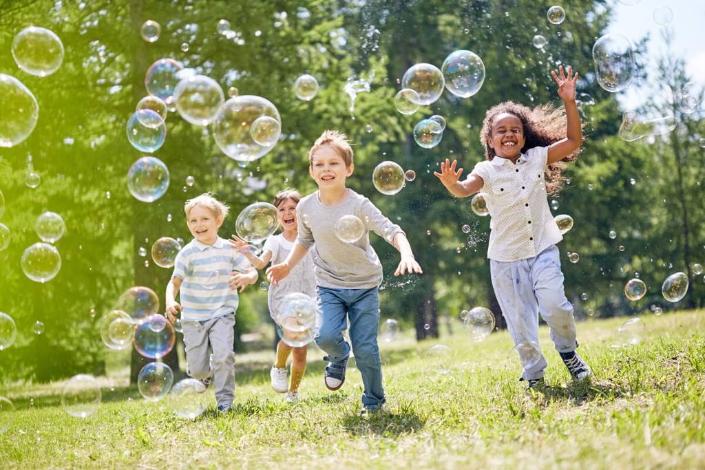 Children running in the park surrounded by bubbles.