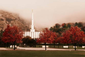 Provo Temple surrounded by red trees and  against a foggy mountain.