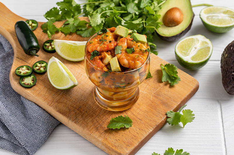 Cutting board with shrimp cocktail and fresh herbs.