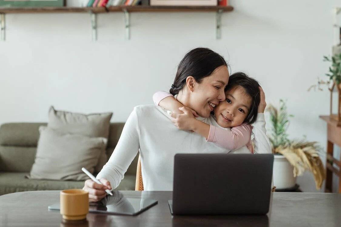 Mother hugging her daughter, at the desk doing work - Photo by Ketut Subiyanto from Pexels