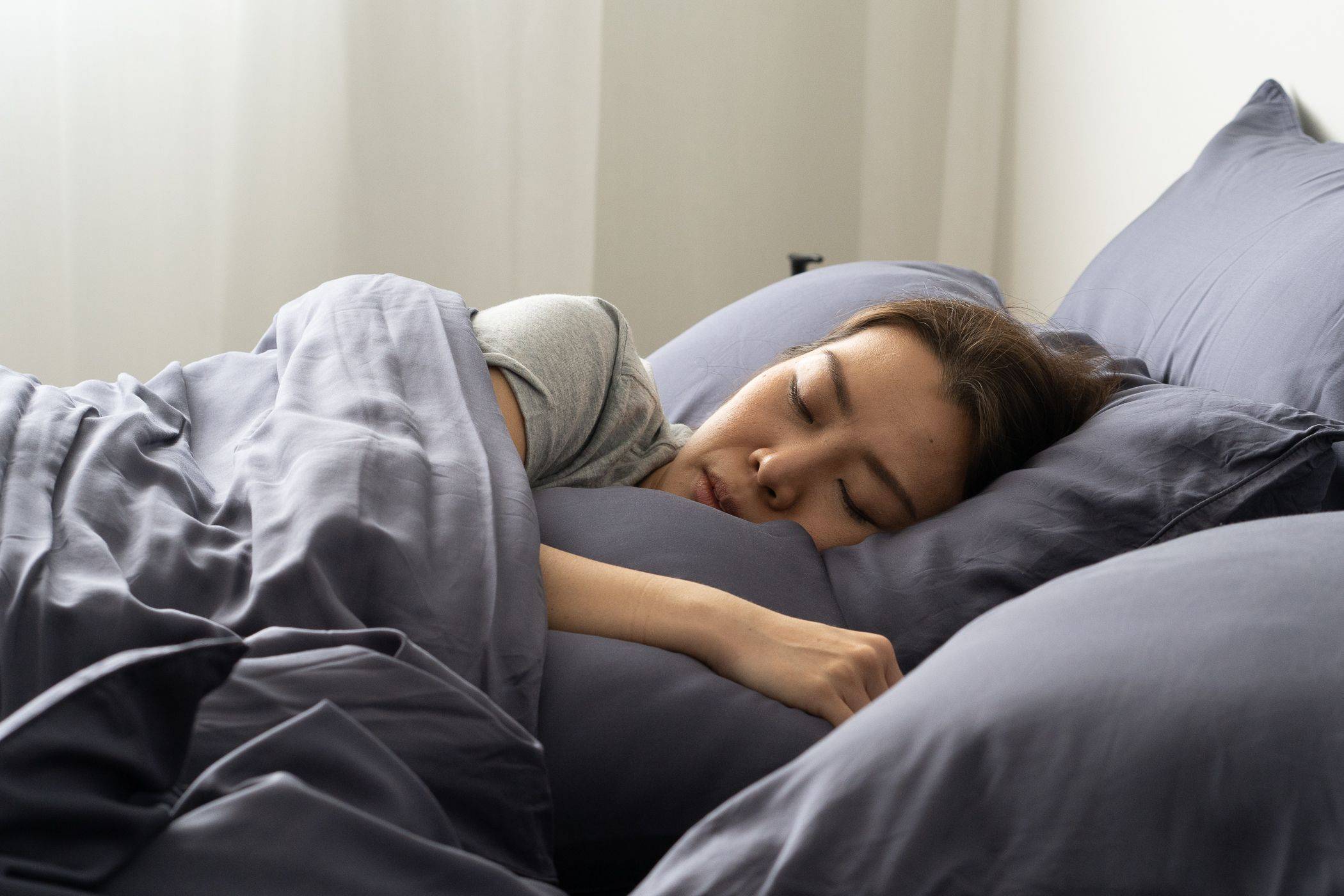 woman sleeping on side on Weavve's  silky tencel lyocell bed sheet set in dark blue 