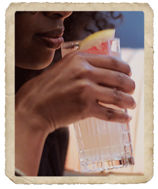 Black girl approaching her lips to a glass with the prepared paloma cocktail