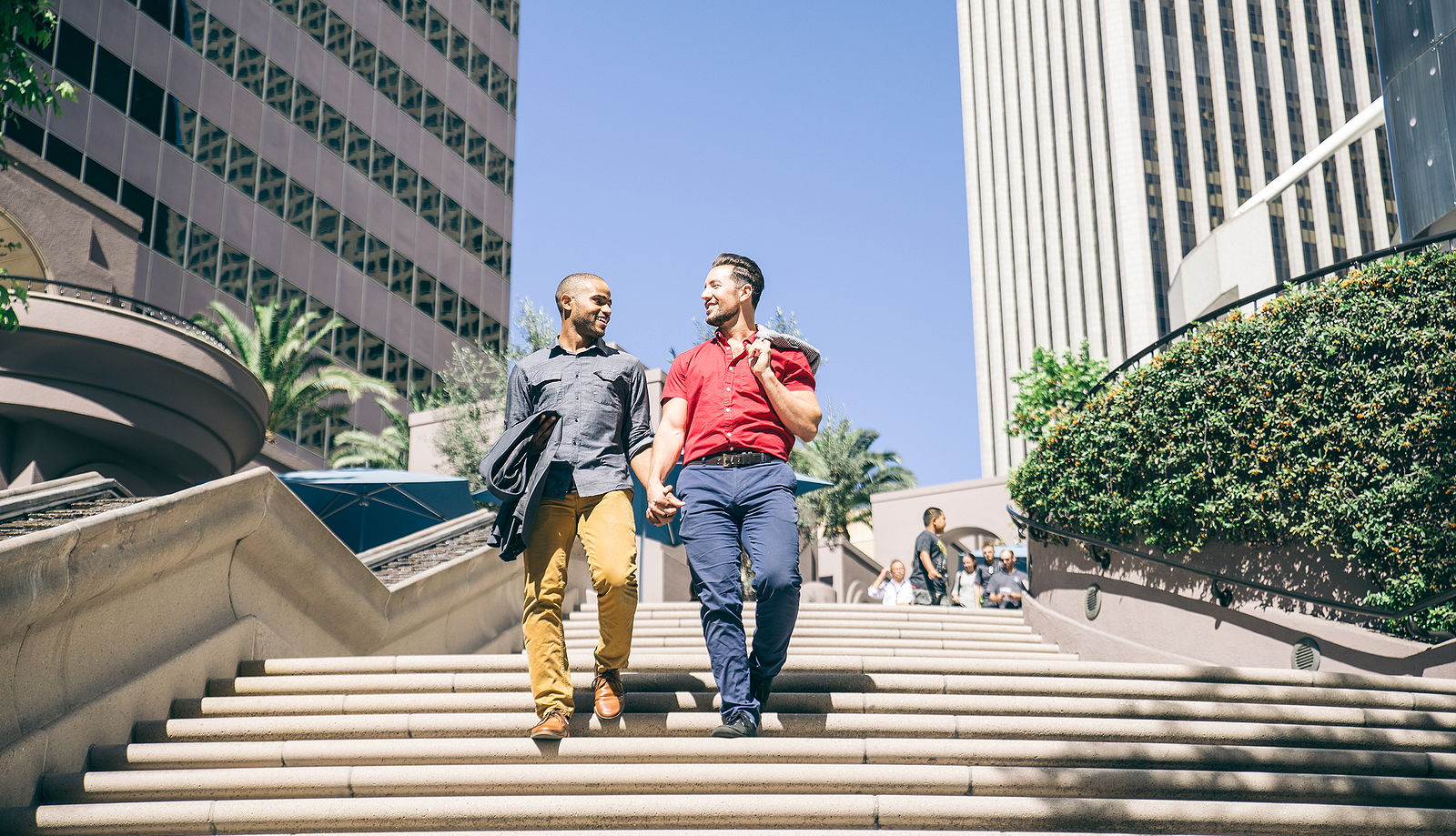 A multi ethnic male couple holding hands and walking down steps together while smiling to eachother.