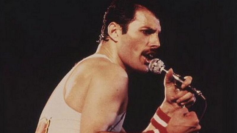 An old image of Freddie with a white wife beater singing deeply into the microphone.