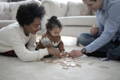 Interracial family sitting on the carpet and playing with wooden blocks toy with their daughter.