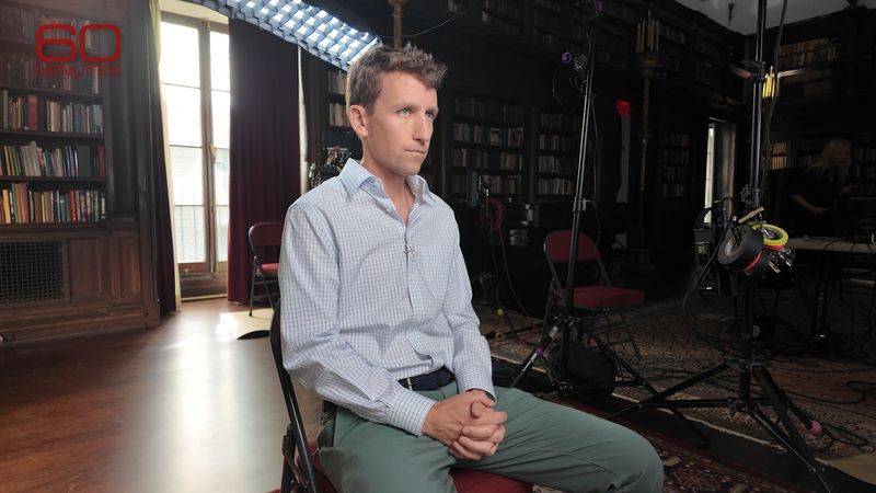 Image may contain: Andrew Dost, Clothing, Shirt, Person, Sitting, Adult, Electrical Device, Microphone, Chair, and Furniture