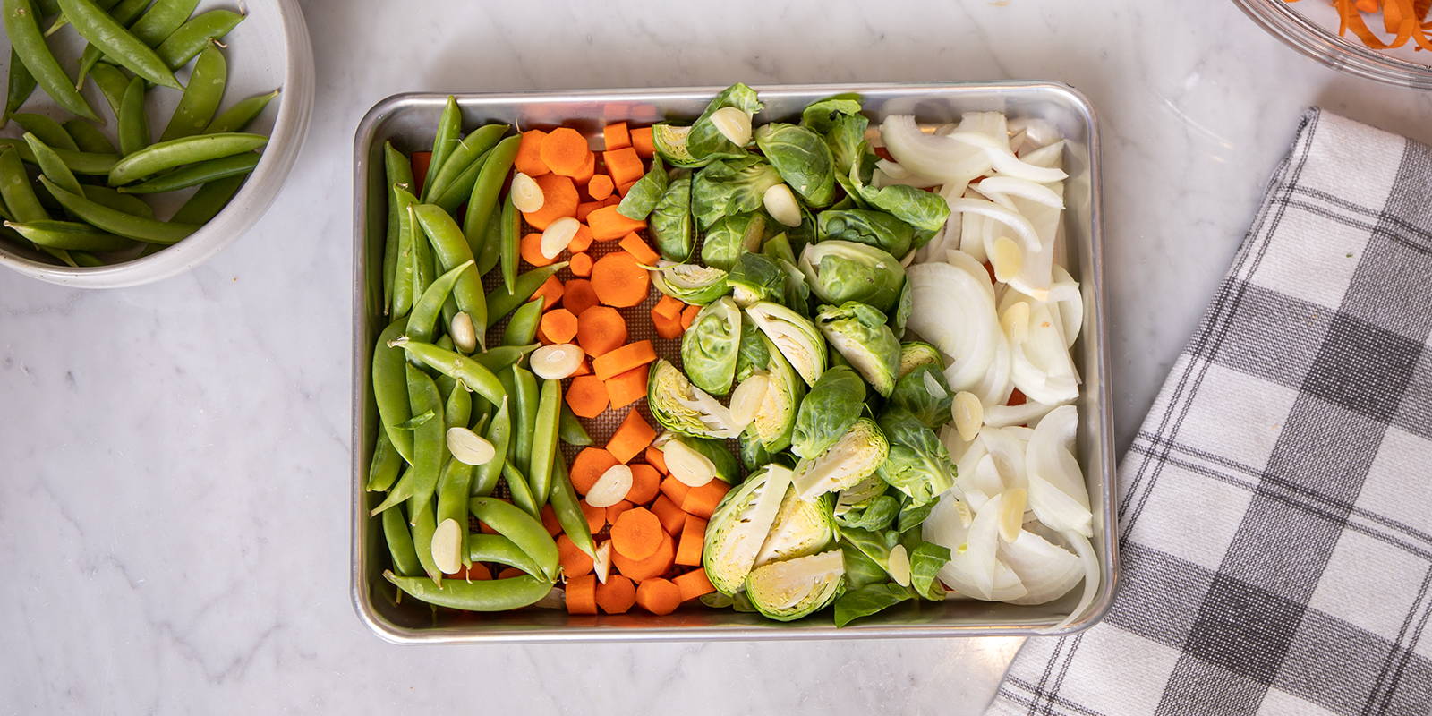 Small sheet pan recipe with vegetables like snow peas, carrots, Brussel sprouts, and onions.