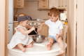 Brother playing cooking with his baby sister on a kitchen table.