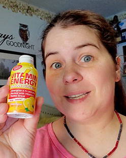 Person holding a bottle of Vitamin Energy drink and smiling.